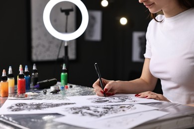 Tattoo artist drawing sketch at table with supplies in salon, closeup