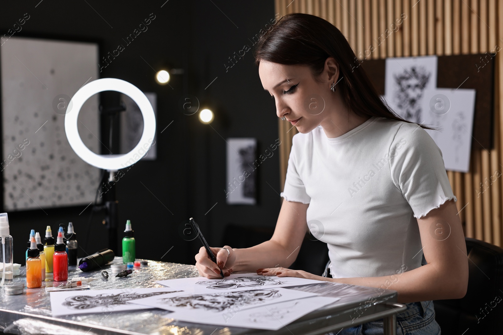 Photo of Tattoo artist drawing sketch at table with supplies in salon