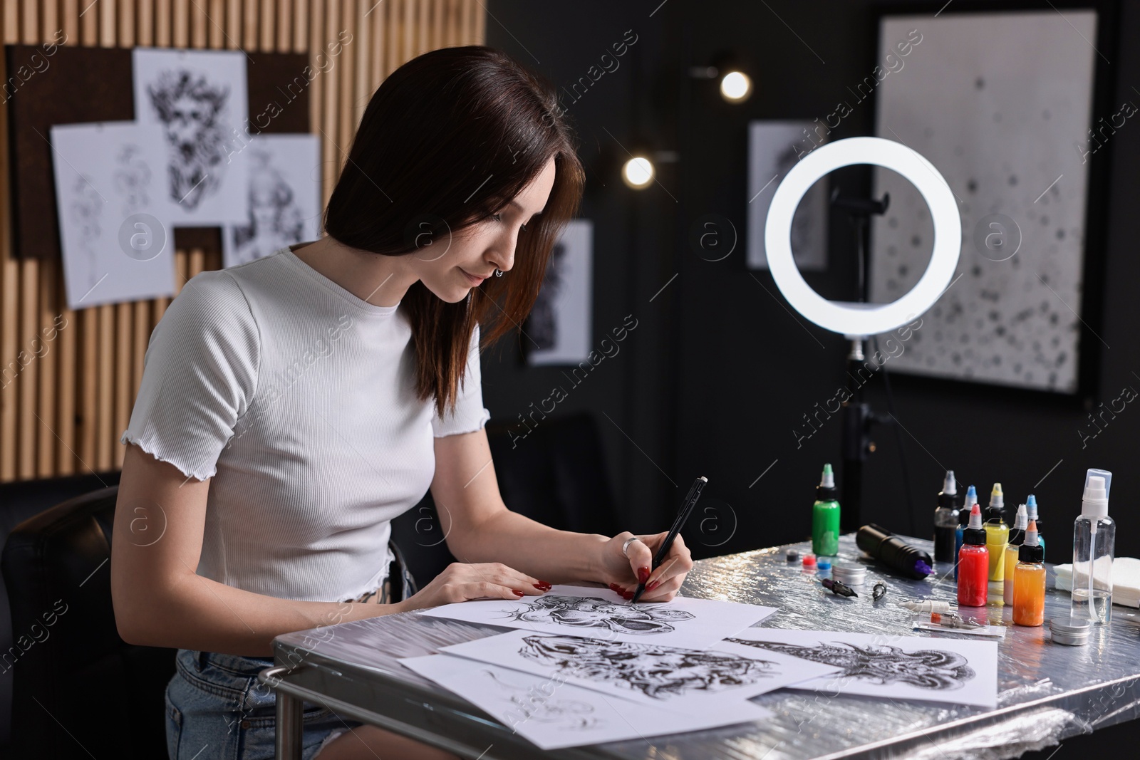 Photo of Tattoo artist drawing sketch at table with supplies in salon