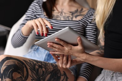 Photo of Tattoo artist showing tablet with sketch to client in salon, closeup