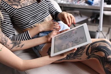 Photo of Tattoo artist showing tablet with sketch to client in salon, closeup