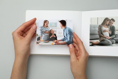 Photo of Woman with open photo album and photos on grey background, top view