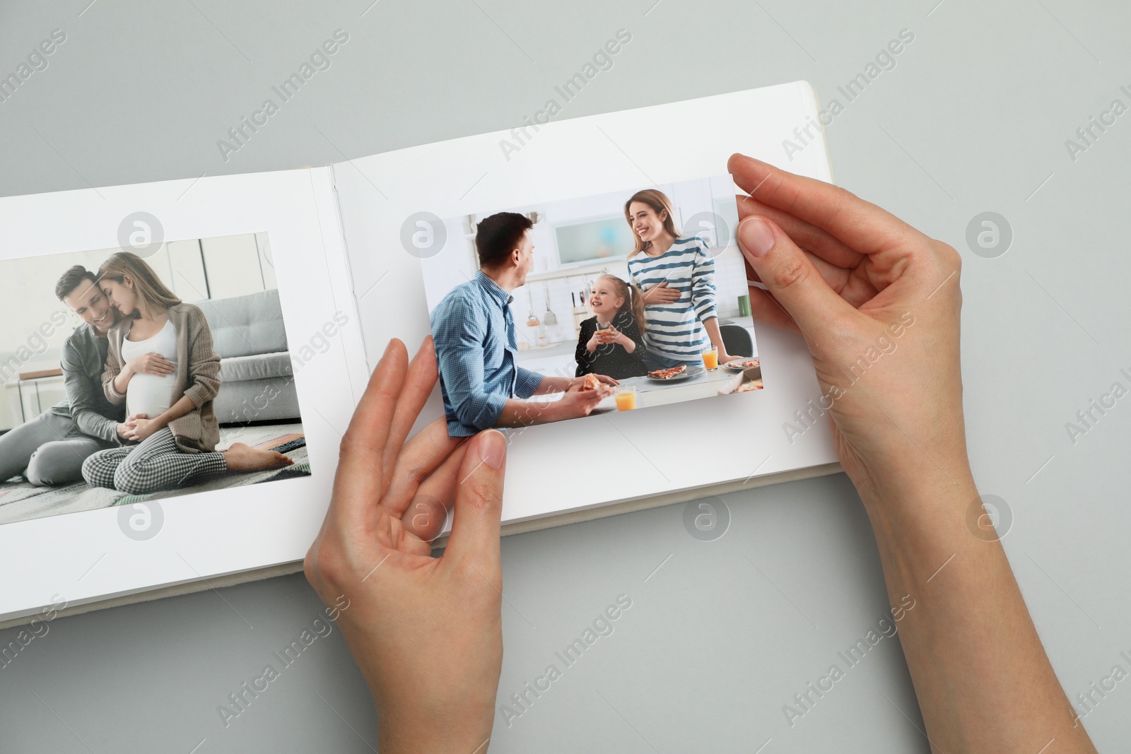 Photo of Woman with open photo album and photos on grey background, top view