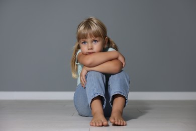 Photo of Orphanage concept. Sad little girl sitting on floor near grey wall