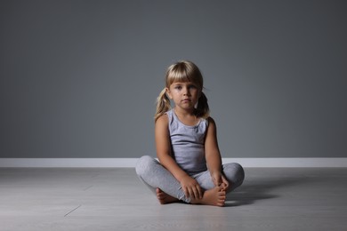 Photo of Orphanage concept. Sad little girl sitting on floor near grey wall