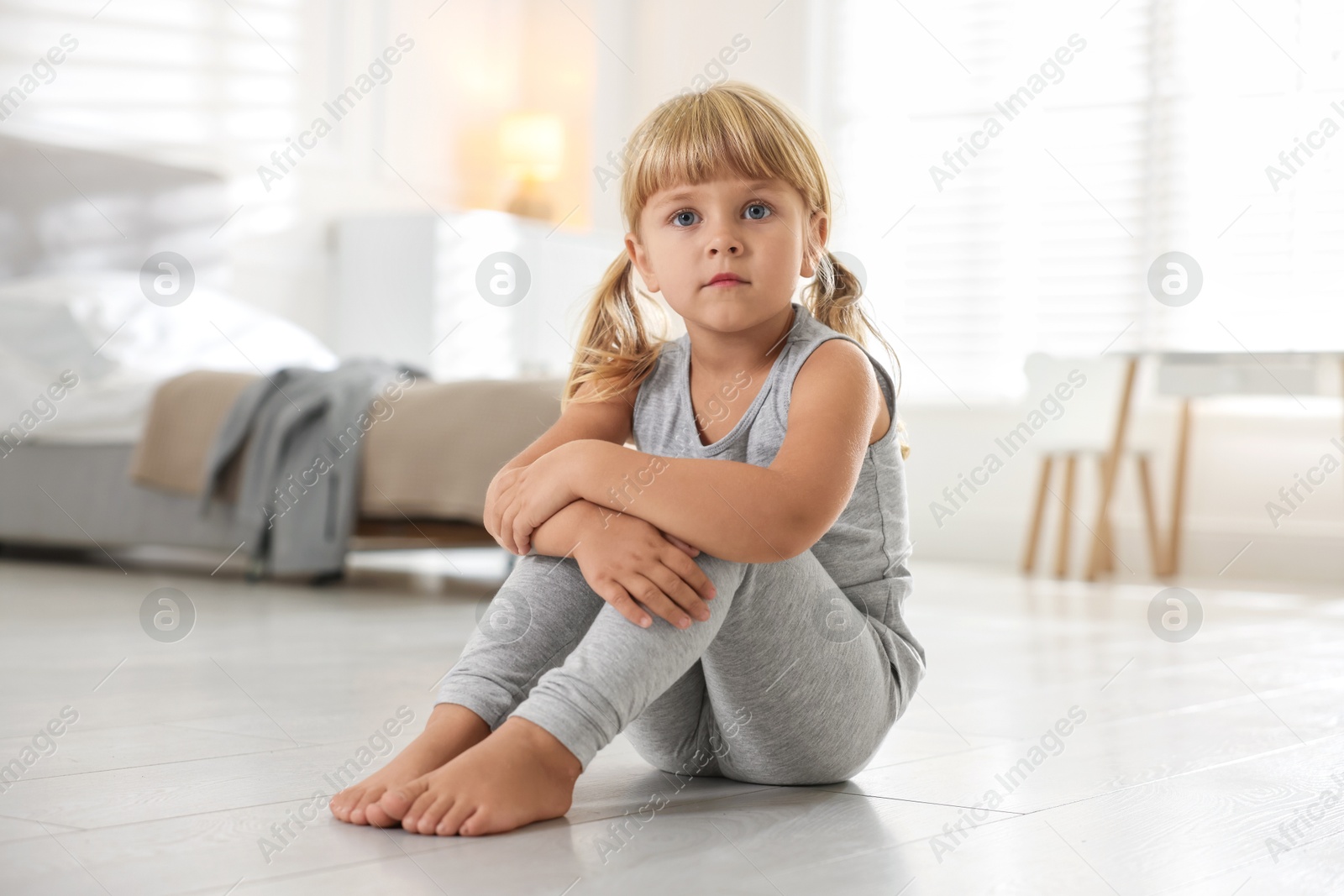 Photo of Orphanage concept. Sad little girl sitting on floor indoors