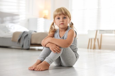 Photo of Orphanage concept. Sad little girl sitting on floor indoors