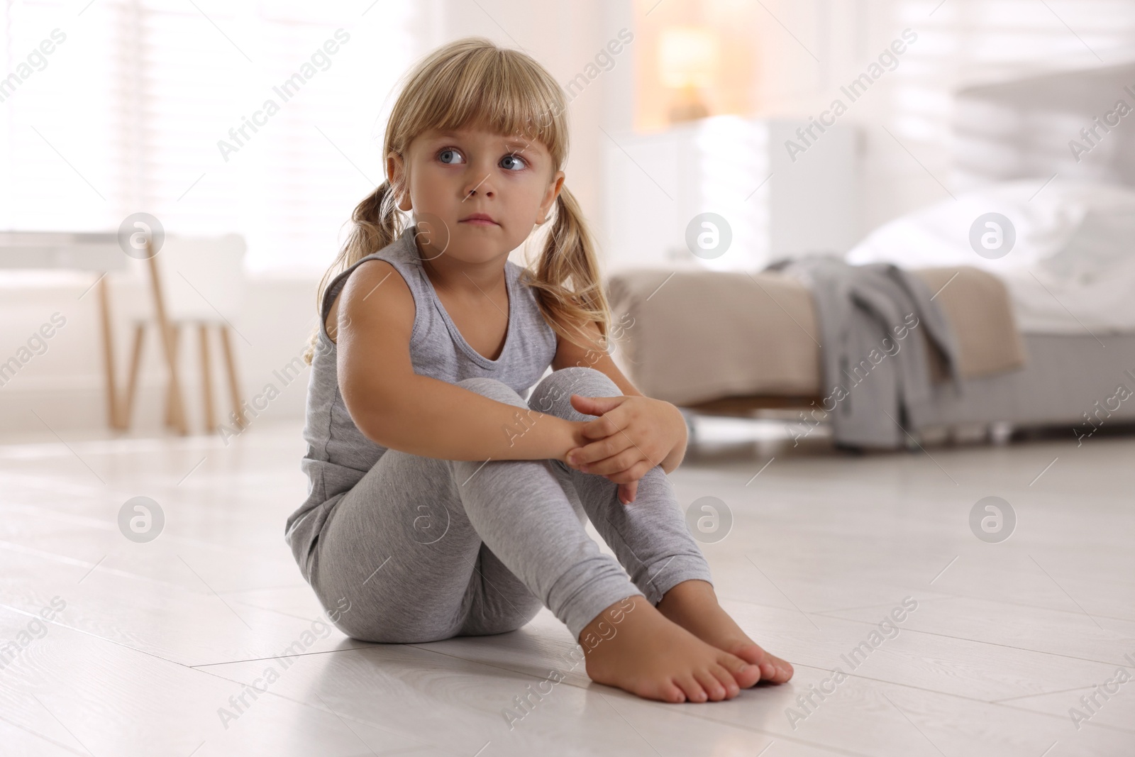 Photo of Orphanage concept. Sad little girl sitting on floor indoors