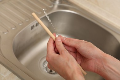 Photo of Woman cleaning bamboo drinking straw with brush in kitchen, closeup