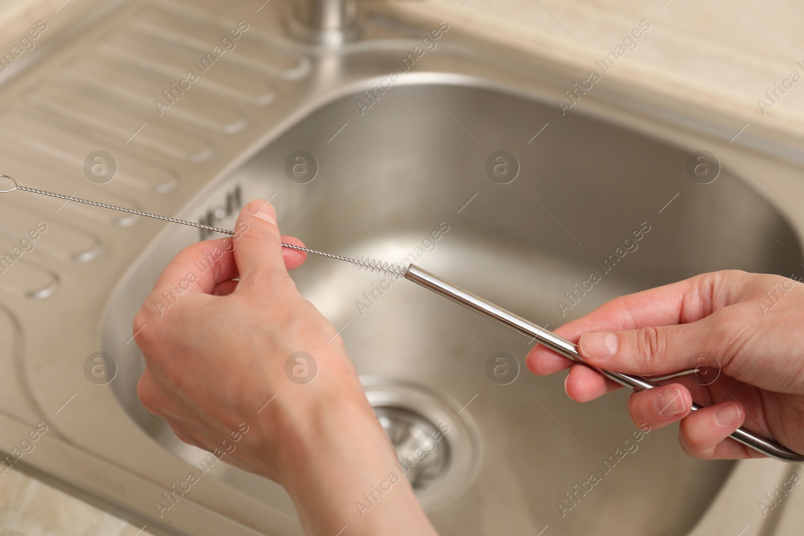 Photo of Woman cleaning metal drinking straw with brush in kitchen, closeup