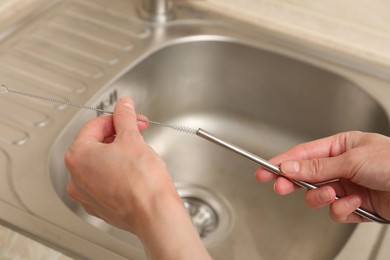 Photo of Woman cleaning metal drinking straw with brush in kitchen, closeup