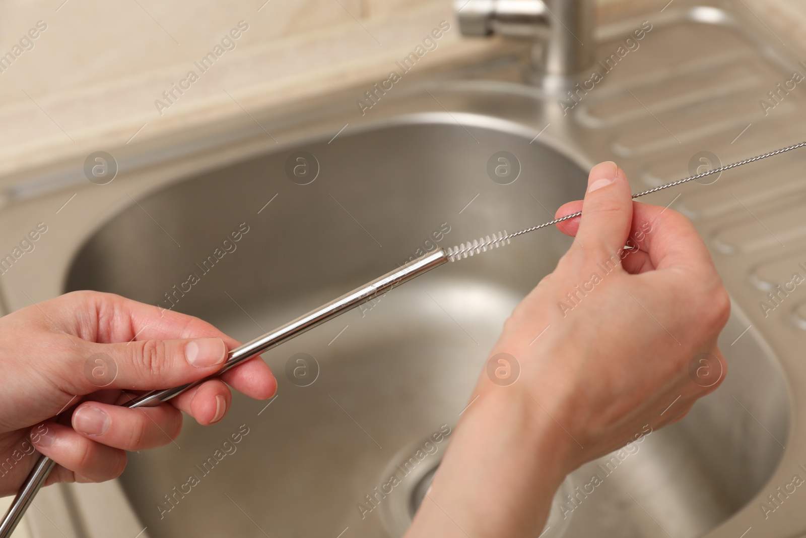 Photo of Woman cleaning metal drinking straw with brush in kitchen, closeup