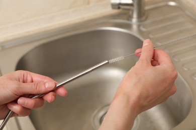 Photo of Woman cleaning metal drinking straw with brush in kitchen, closeup