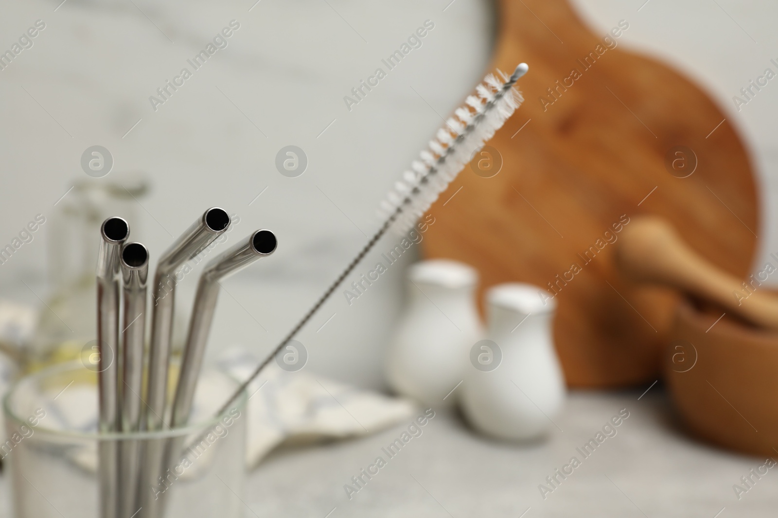 Photo of Metal drinking straws and cleaning brush in glass in kitchen, closeup. Space for text