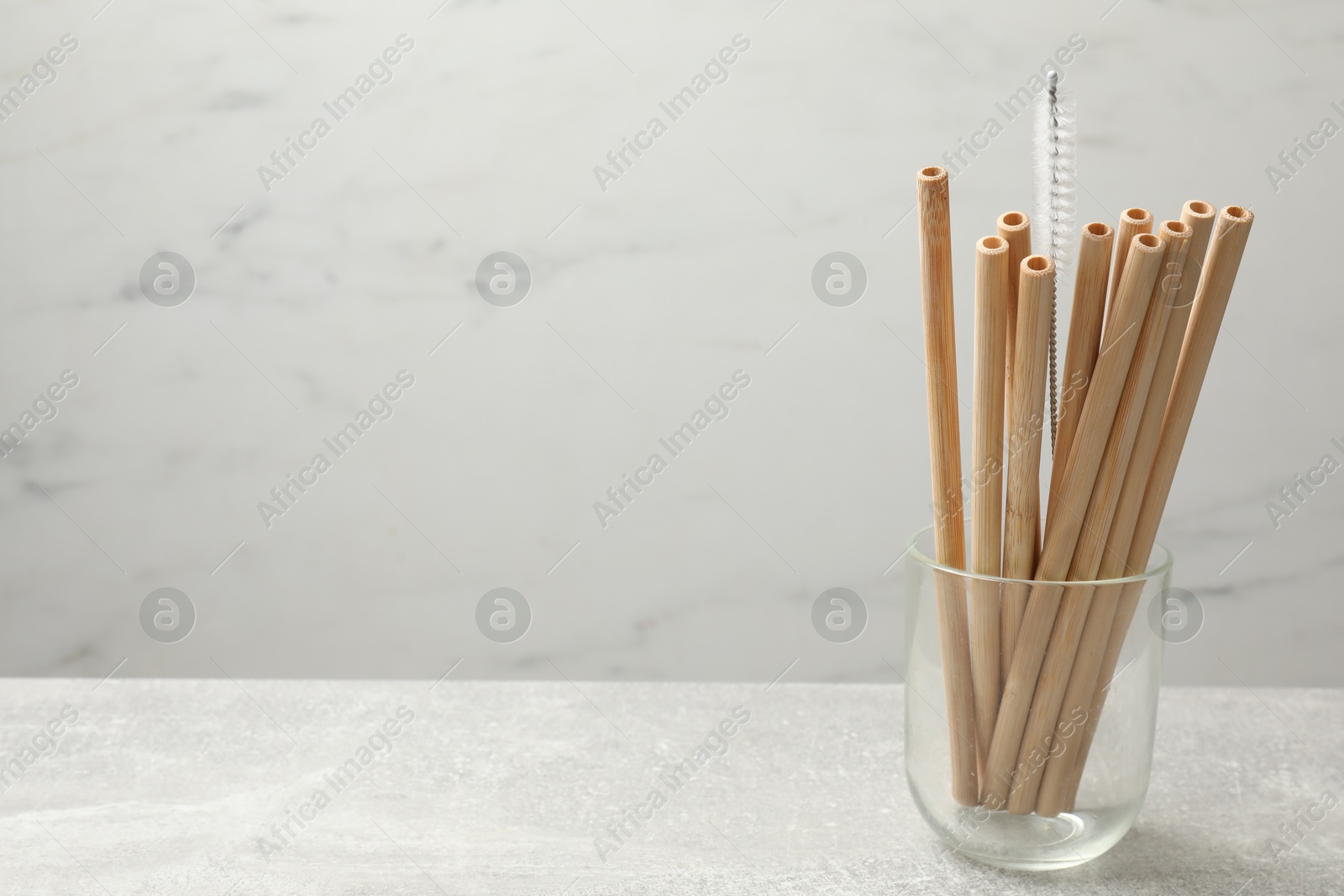 Photo of Bamboo drinking straws and cleaning brush in glass on light table, space for text