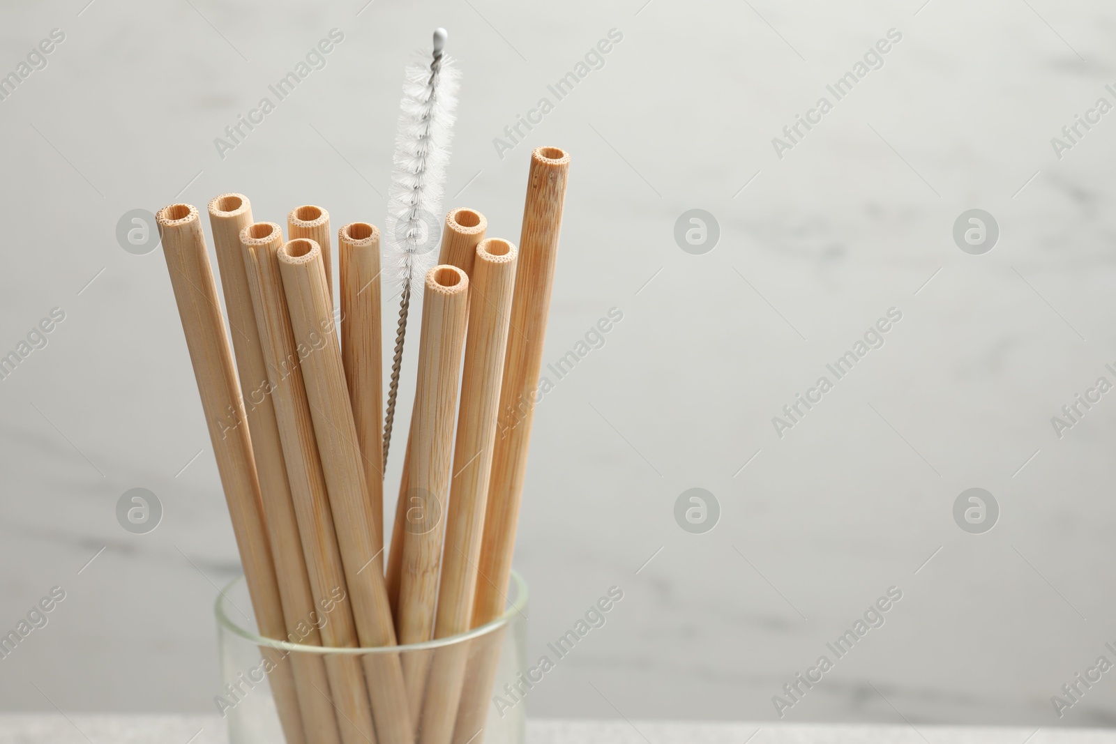 Photo of Bamboo drinking straws and cleaning brush in glass on blurred background, closeup. Space for text