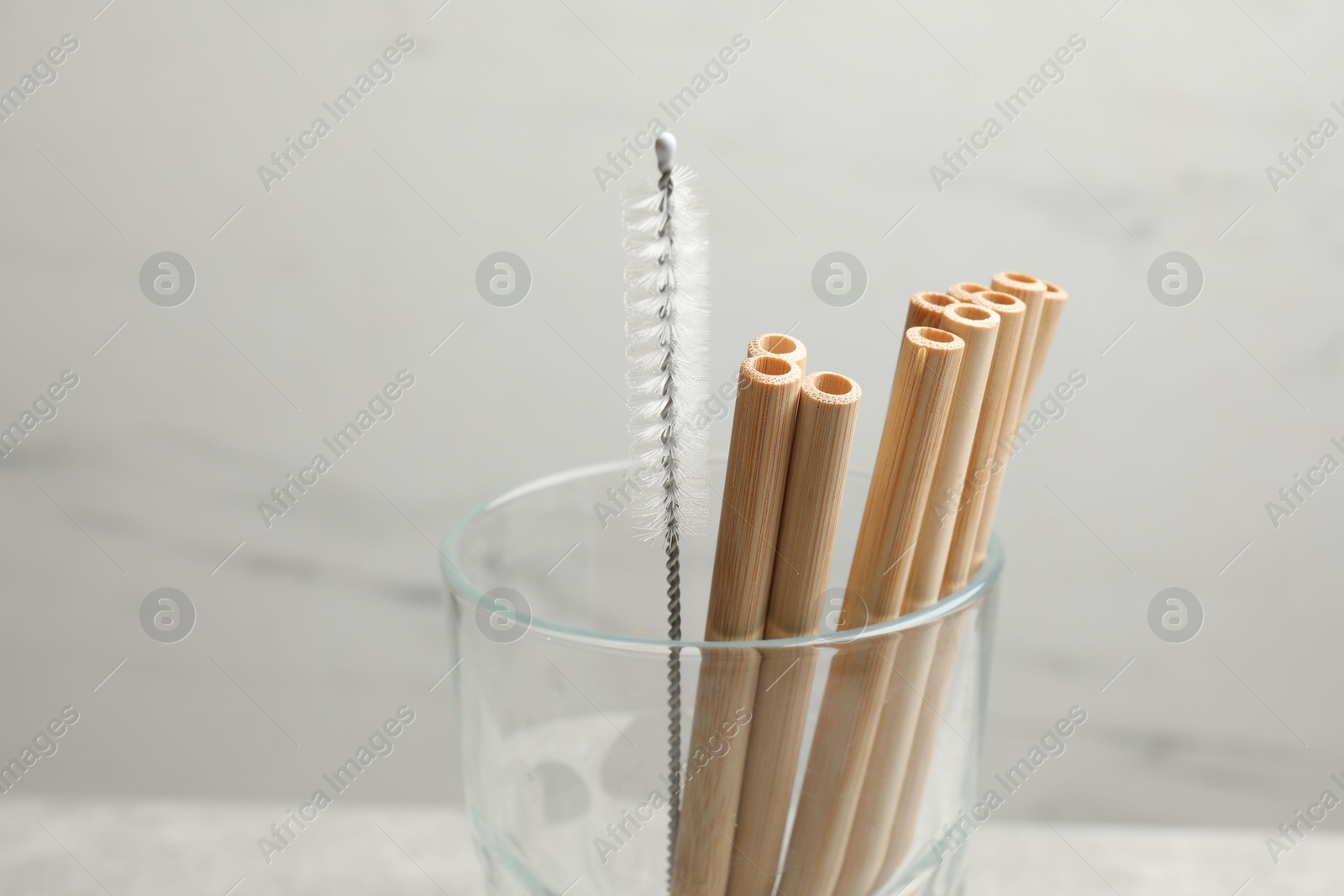 Photo of Bamboo drinking straws and cleaning brush in glass on blurred background, closeup