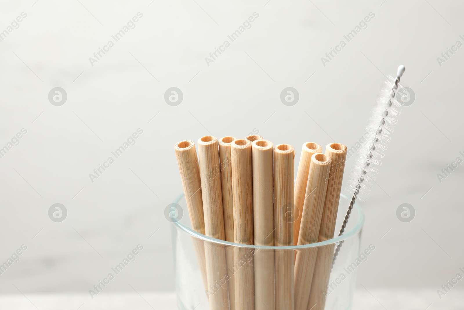 Photo of Bamboo drinking straws and cleaning brush in glass on blurred background, closeup