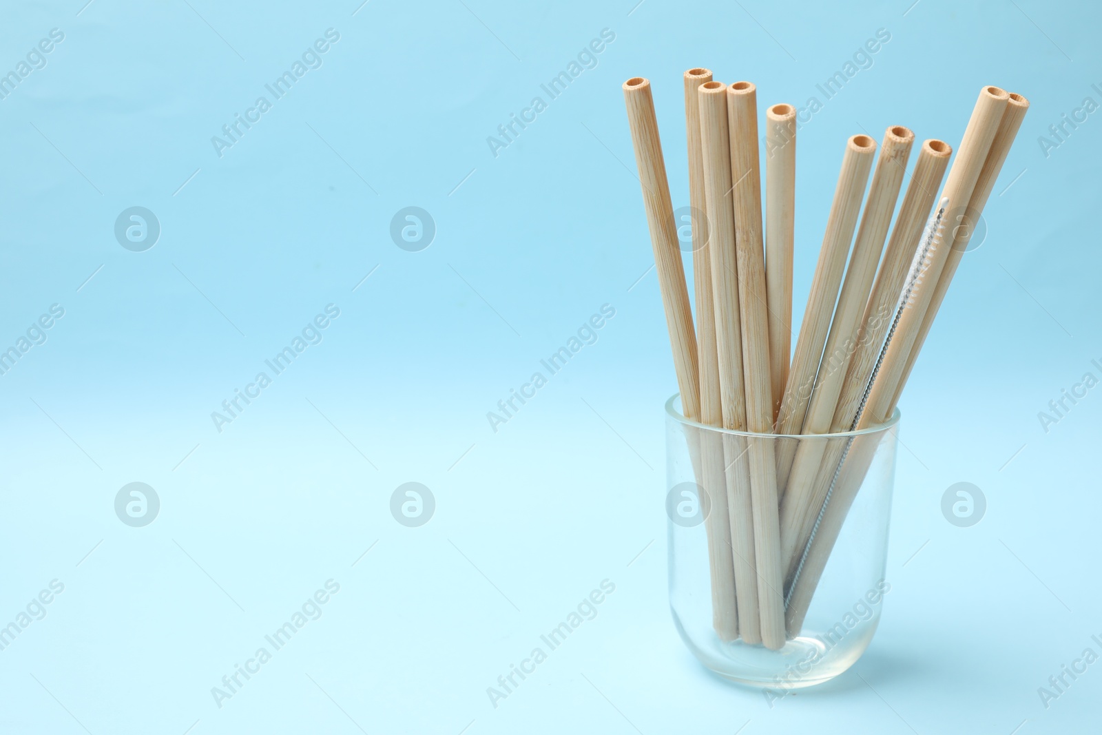 Photo of Bamboo drinking straws and cleaning brush in glass on light blue background. Space for text