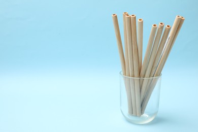 Photo of Bamboo drinking straws and cleaning brush in glass on light blue background. Space for text