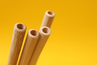 Photo of Bamboo drinking straws on yellow background, closeup. Space for text