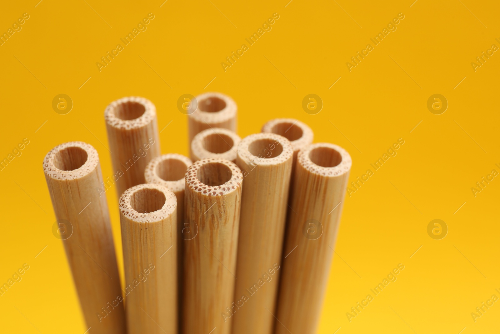 Photo of Bamboo drinking straws on yellow background, closeup