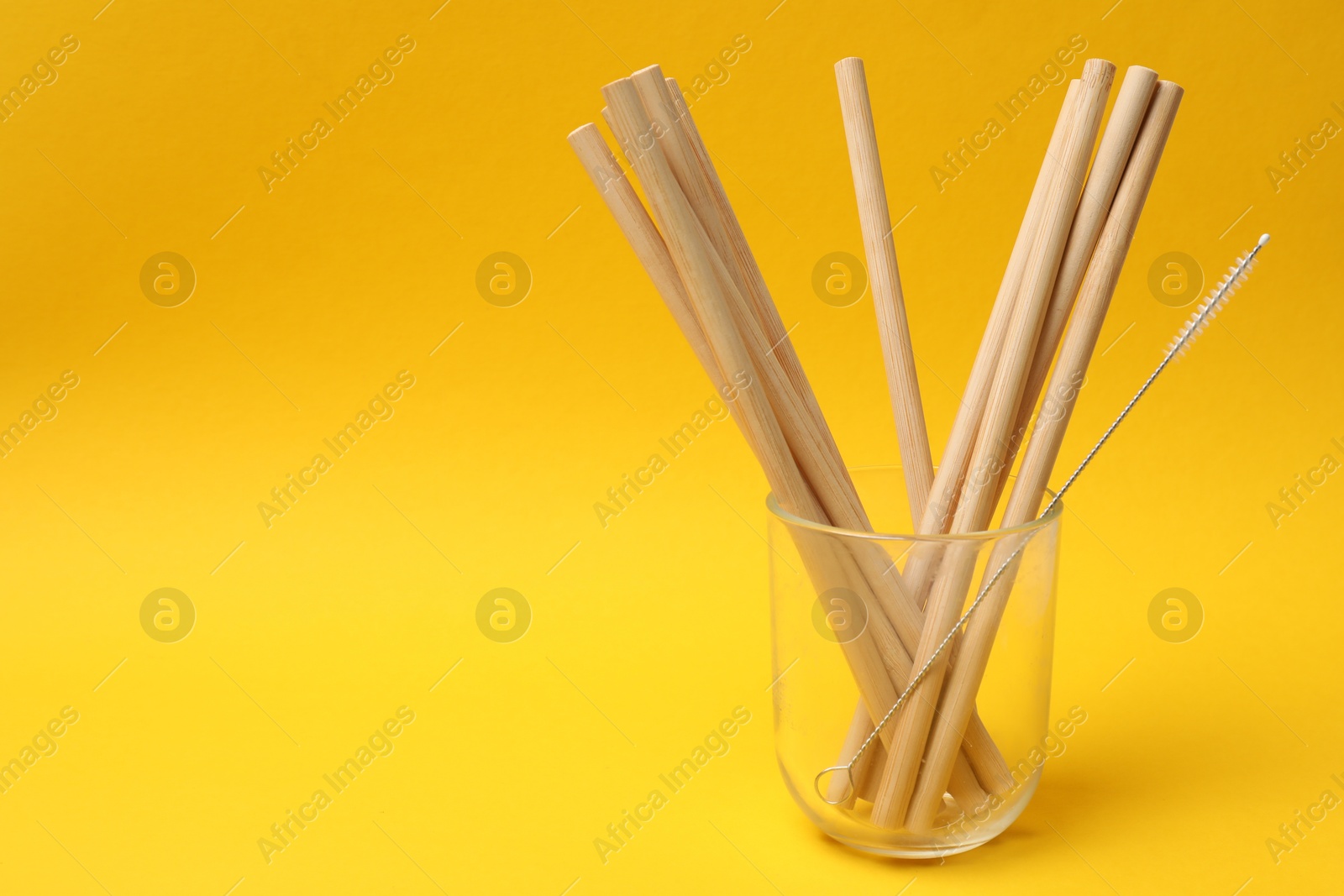 Photo of Bamboo drinking straws and cleaning brush in glass on yellow background. Space for text