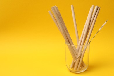 Photo of Bamboo drinking straws and cleaning brush in glass on yellow background. Space for text