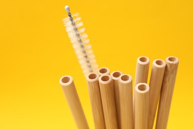 Photo of Bamboo drinking straws and cleaning brush on yellow background, closeup