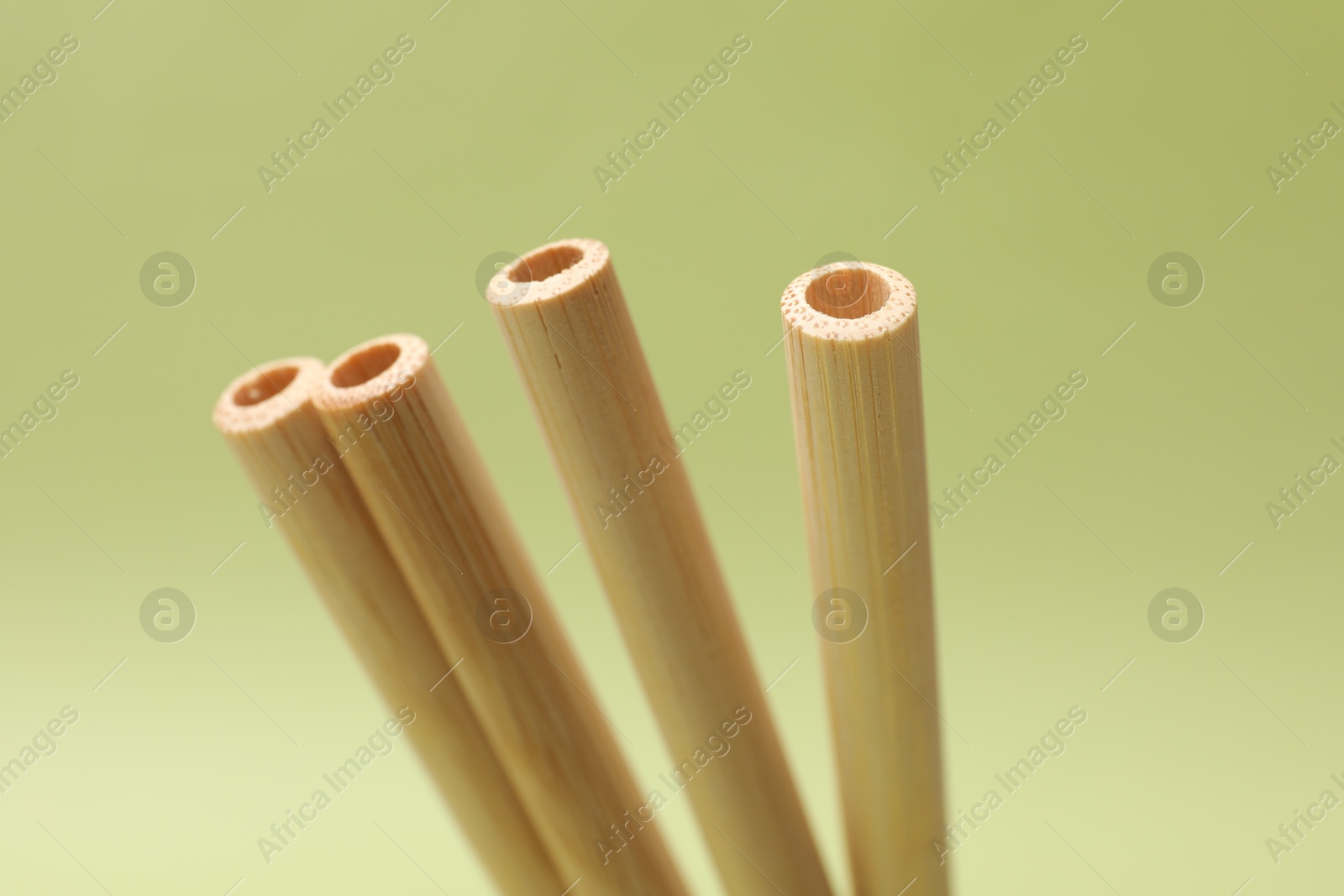 Photo of Bamboo drinking straws on light green background, closeup