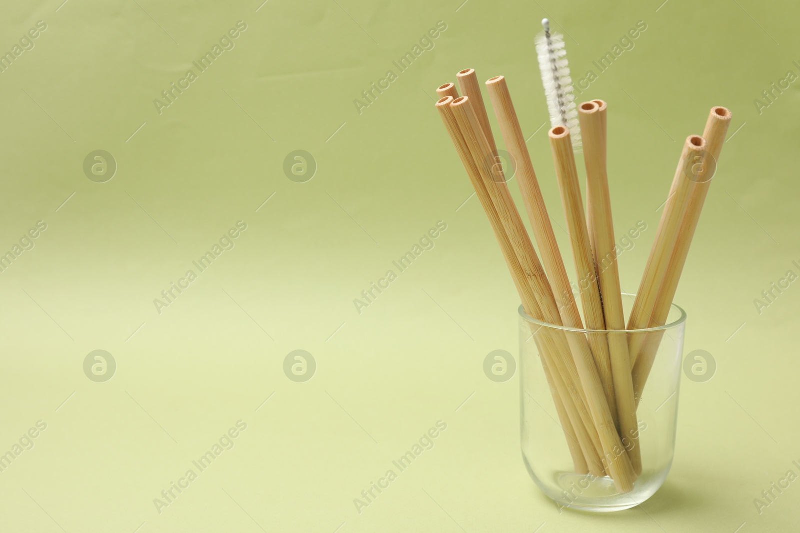 Photo of Bamboo drinking straws and cleaning brush in glass on light green background. Space for text