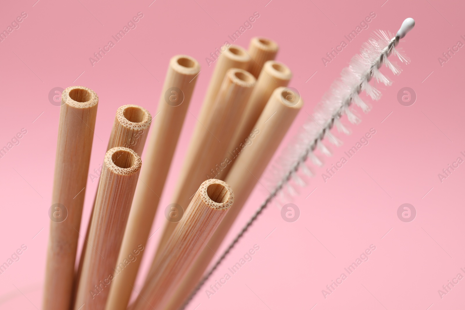 Photo of Bamboo drinking straws and cleaning brush on pink background, closeup