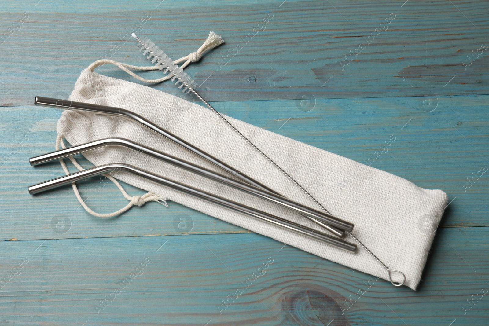 Photo of Metal drinking straws, bag and cleaning brush on light blue wooden table, top view