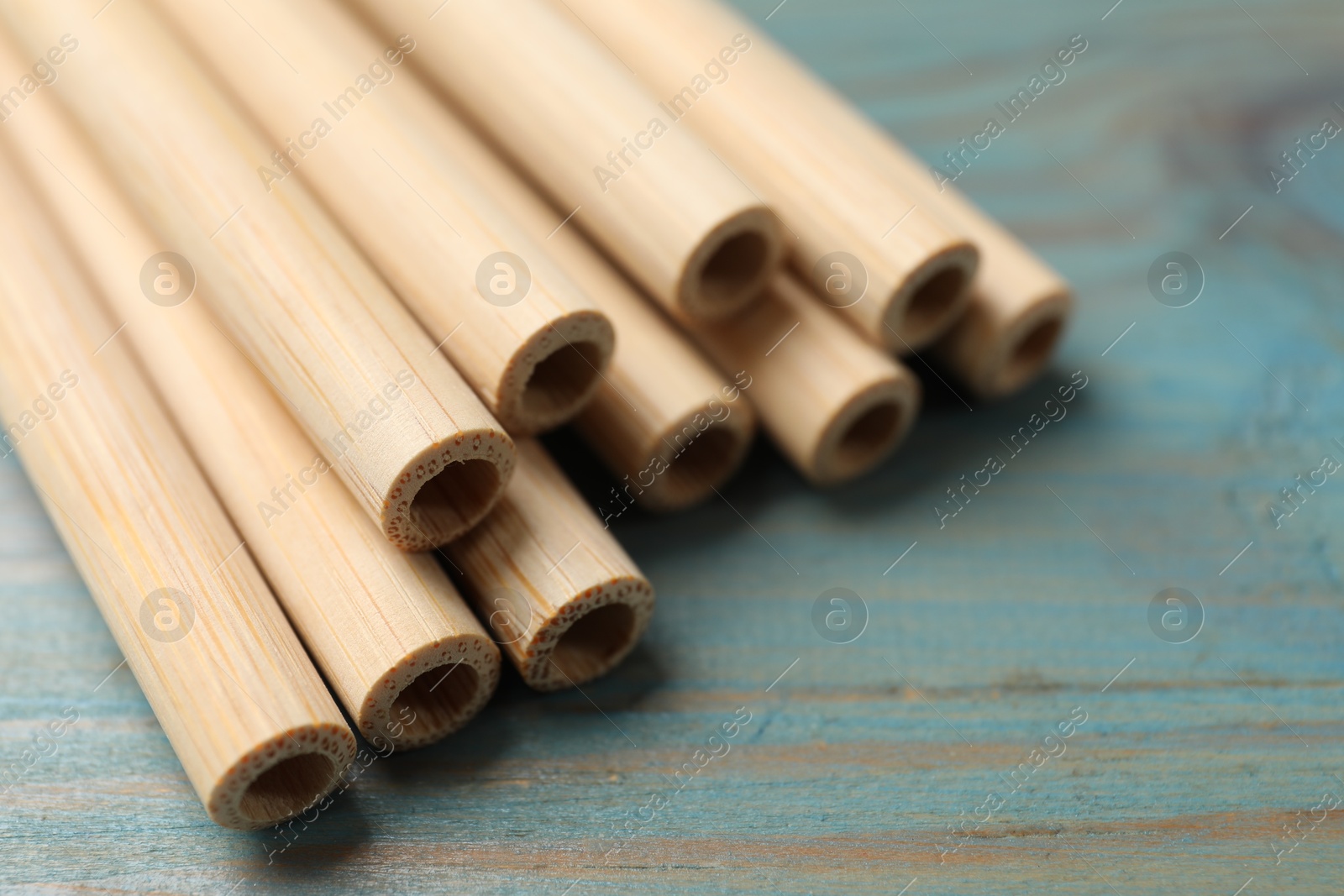 Photo of Bamboo drinking straws on light blue wooden table, closeup