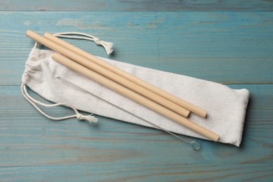 Photo of Bamboo drinking straws, cleaning brush and bag on light blue wooden table, top view