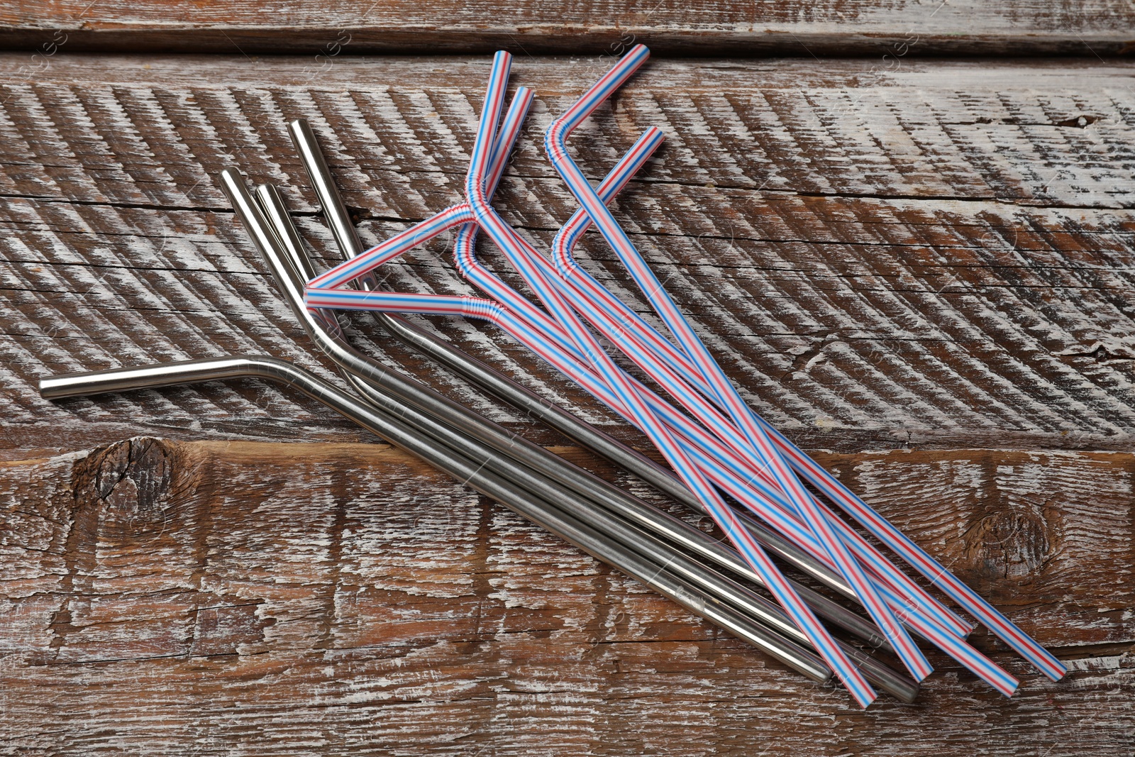 Photo of Different drinking straws on wooden table, flat lay