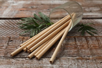 Photo of Bamboo drinking straws in glass and green leaves on wooden table, closeup