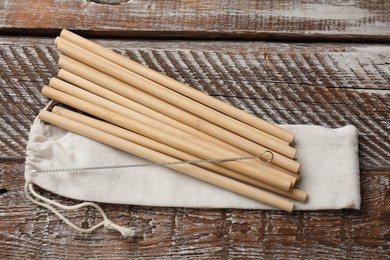 Photo of Bamboo drinking straws, cleaning brush and bag on wooden table, top view