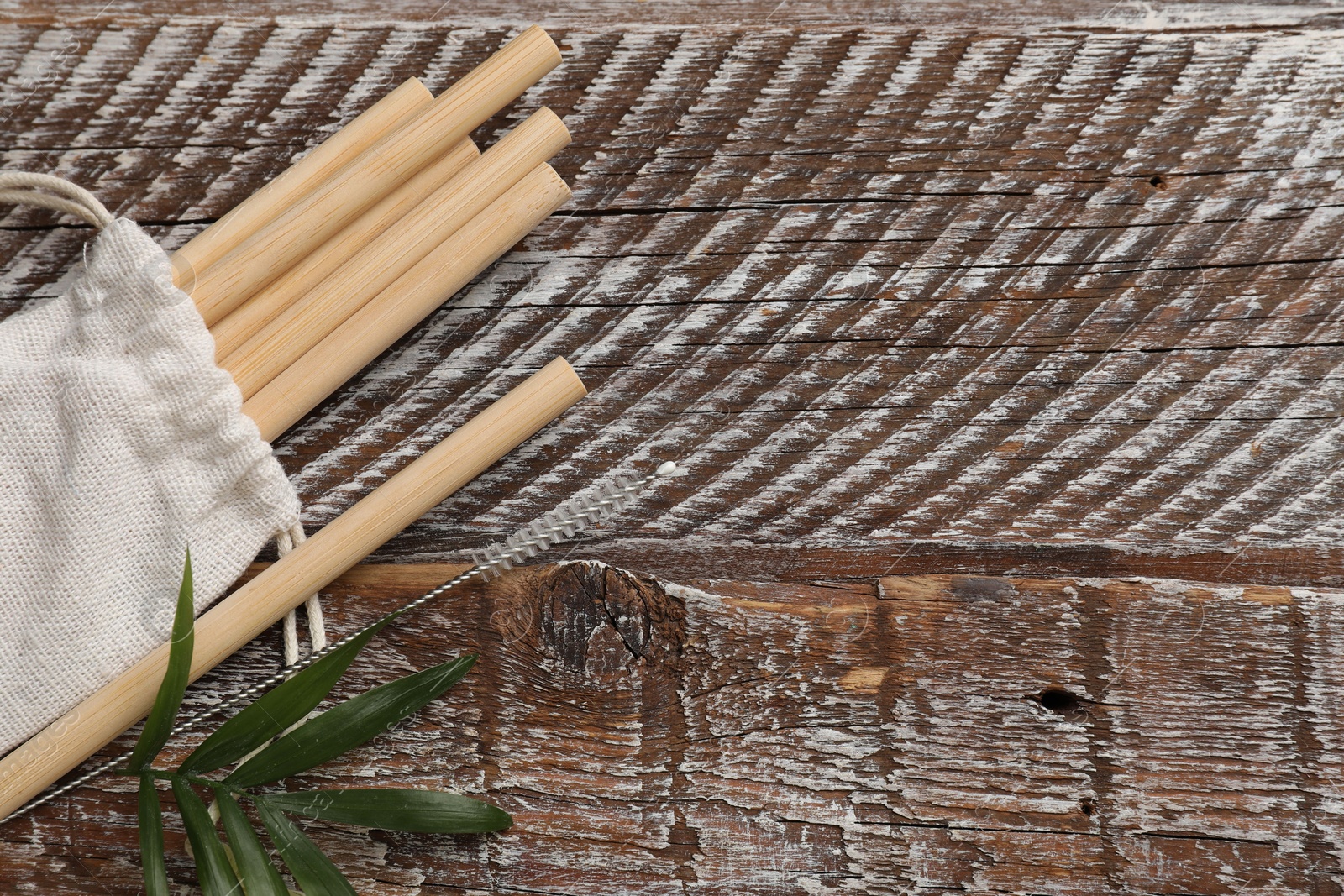 Photo of Bamboo drinking straws, cleaning brush and bag on wooden table, top view. Space for text