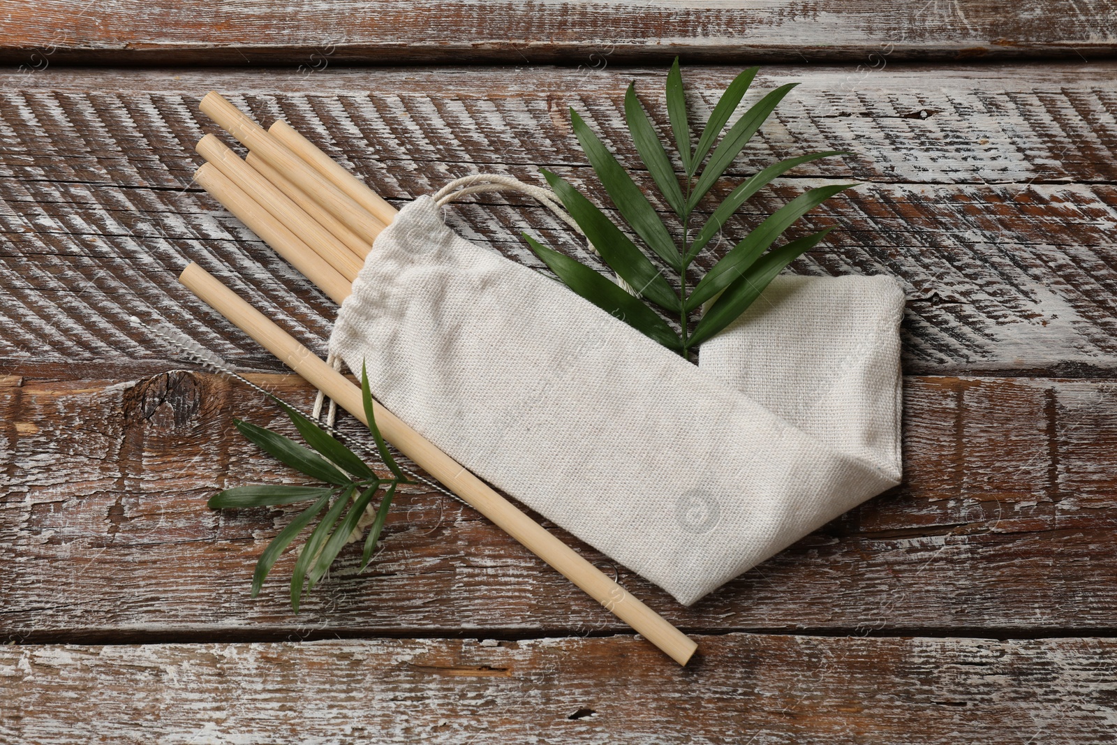 Photo of Bamboo drinking straws, cleaning brush and bag on wooden table, top view