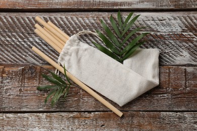 Photo of Bamboo drinking straws, cleaning brush and bag on wooden table, top view