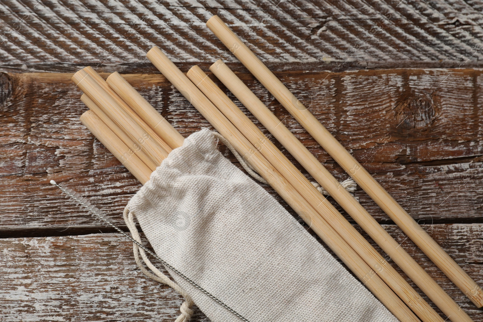 Photo of Bamboo drinking straws, cleaning brush and bag on wooden table, top view