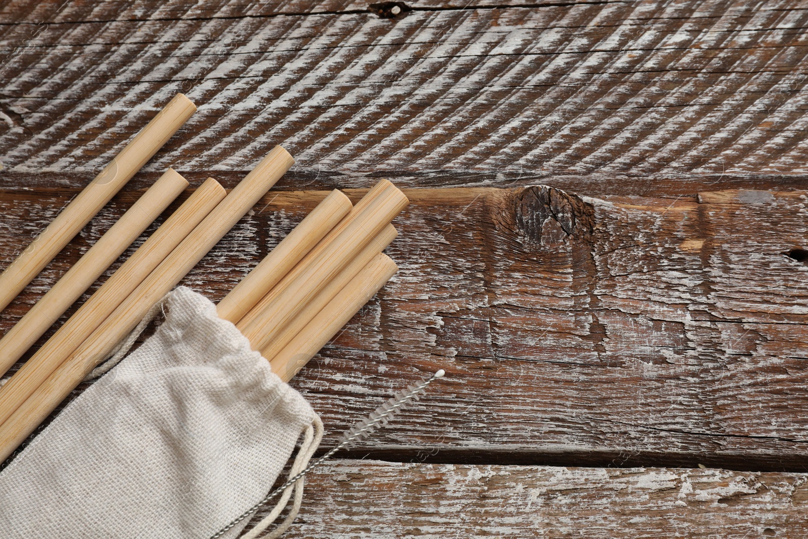 Photo of Bamboo drinking straws, cleaning brush and bag on wooden table, top view. Space for text