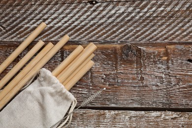 Photo of Bamboo drinking straws, cleaning brush and bag on wooden table, top view. Space for text