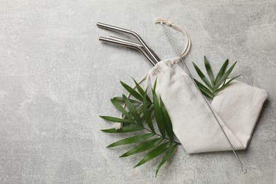 Photo of Metal drinking straws in bag, cleaning brush and leaves on grey textured table, top view. space for text