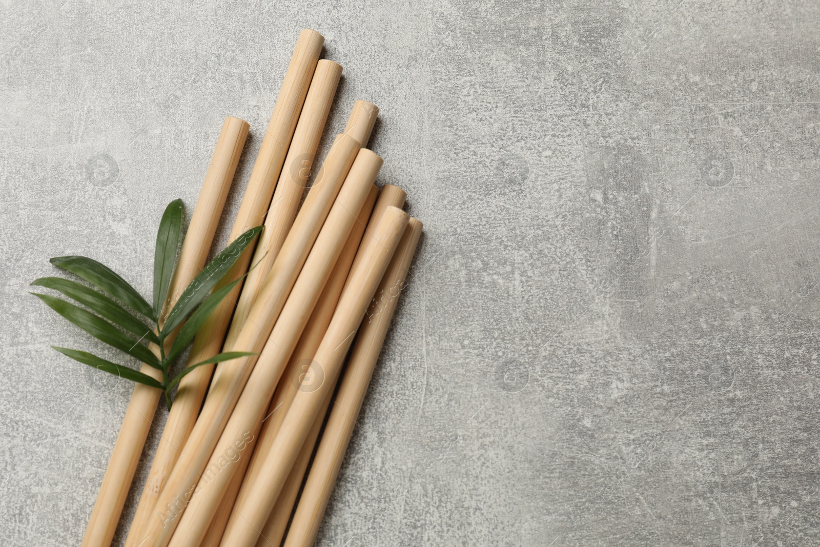 Photo of Bamboo drinking straws and green leaves on grey textured table, top view. Space for text