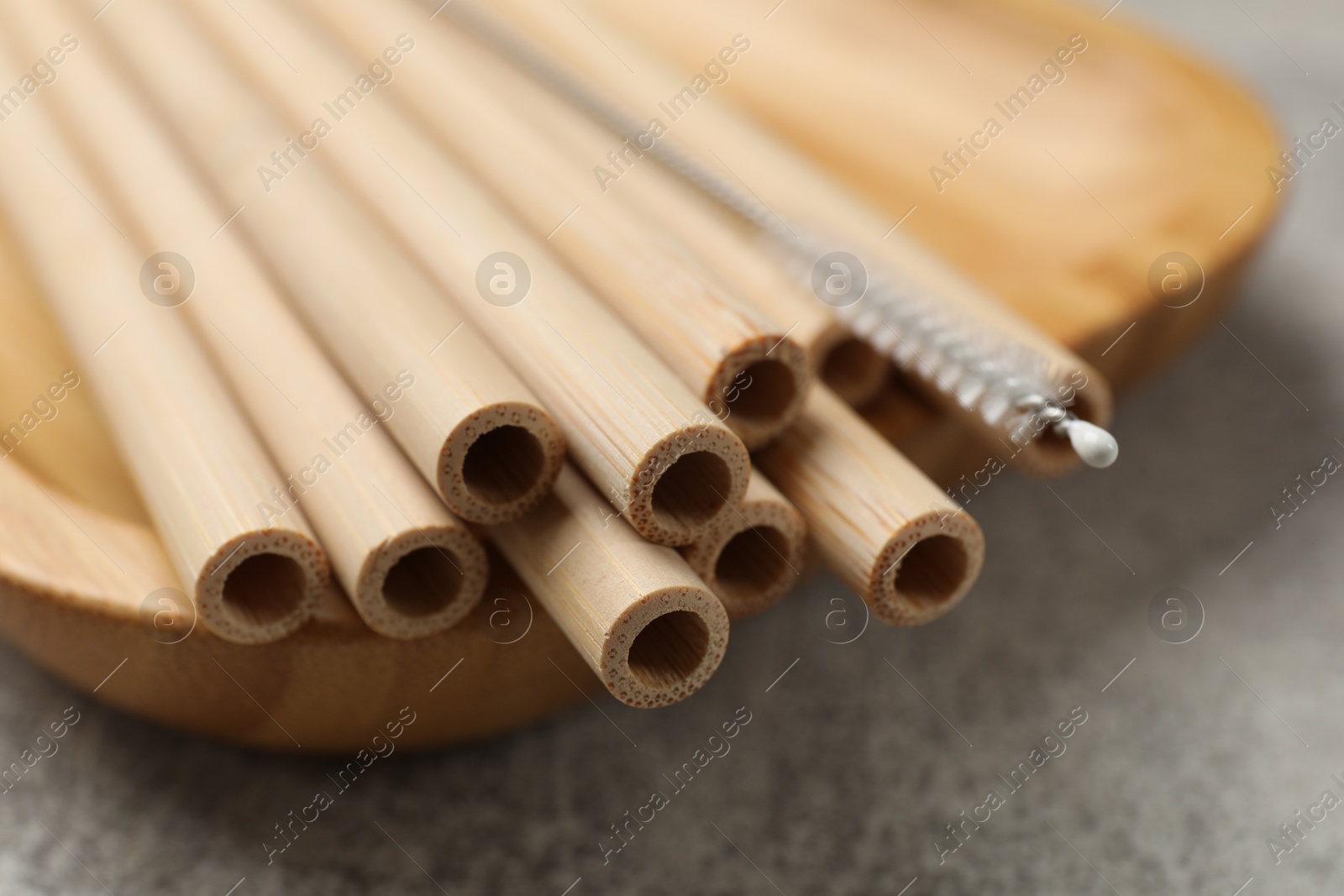 Photo of Bamboo drinking straws and cleaning brush on grey textured table, closeup