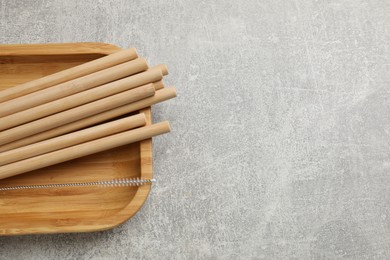 Photo of Bamboo drinking straws and cleaning brush on grey textured table, top view. Space for text