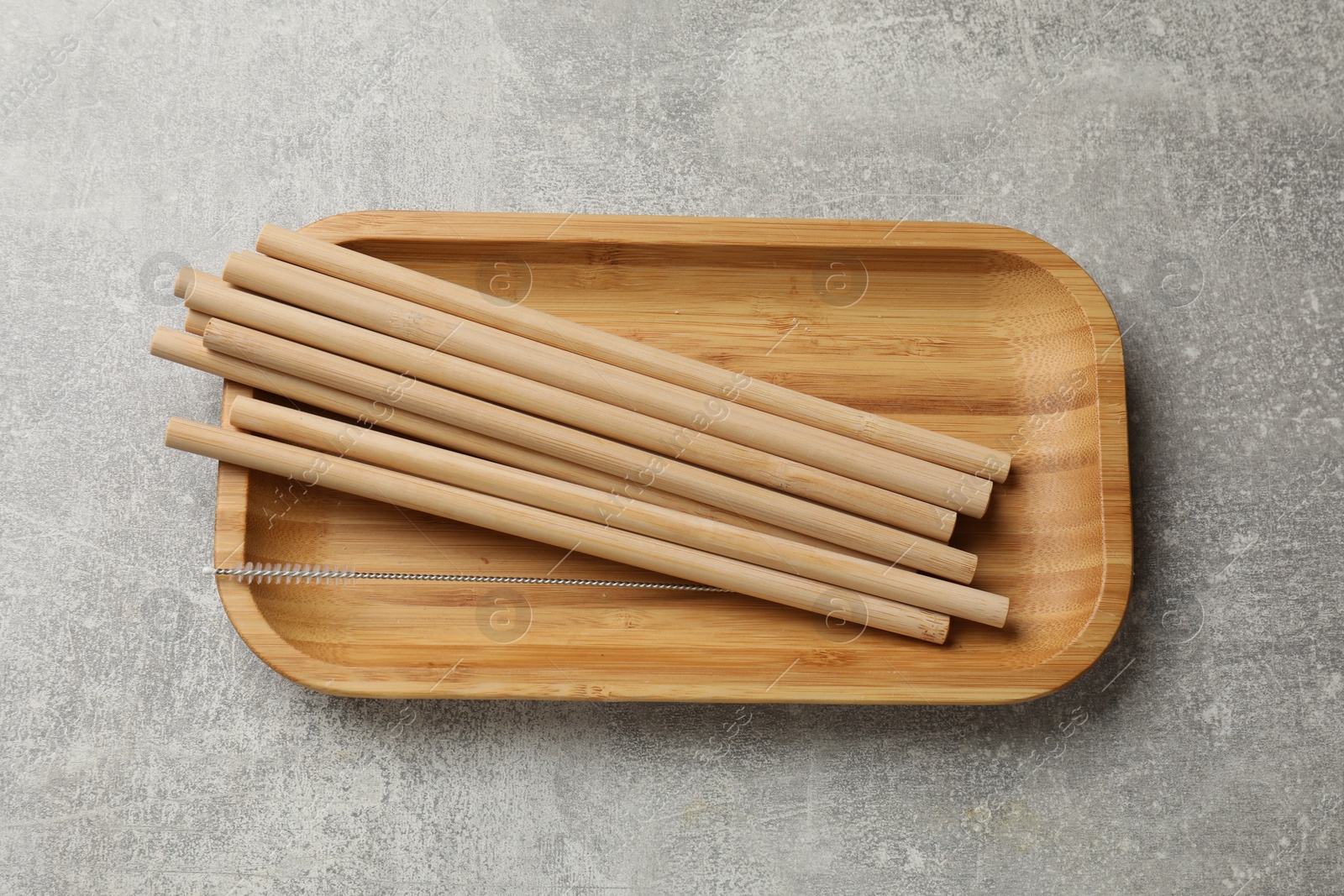 Photo of Bamboo drinking straws and cleaning brush on grey textured table, top view