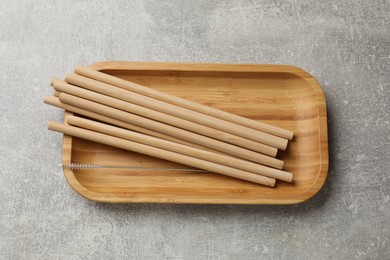 Photo of Bamboo drinking straws and cleaning brush on grey textured table, top view